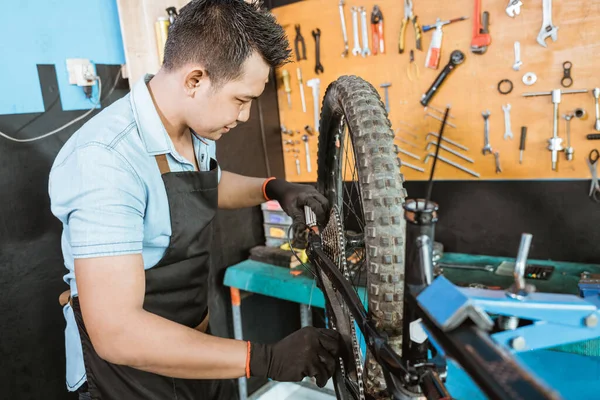 Male bicycle mechanic in apron lubricating chain while repairing problem on bicycle — Φωτογραφία Αρχείου