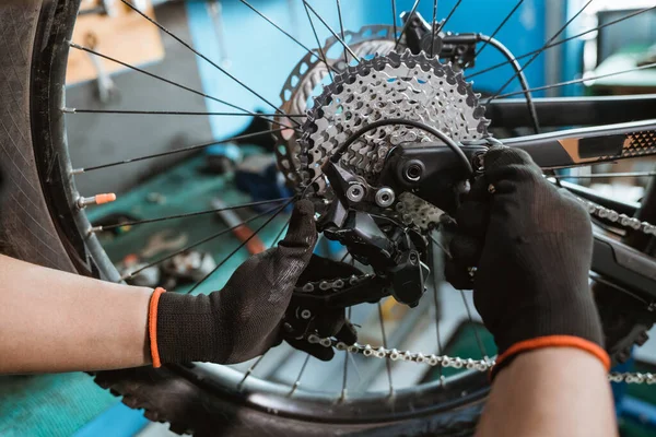 male bicycle mechanics hand in gloves attaches chain over sprocket