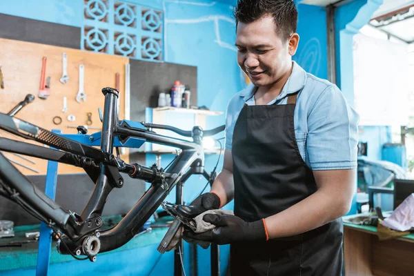 Un mecánico de bicicleta en delantal sostiene el juego de manivela mientras lo instala en una bicicleta nueva —  Fotos de Stock