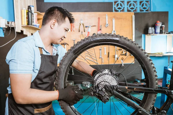 Un mecánico de bicicleta en delantal instala ejes al instalar ruedas de bicicleta —  Fotos de Stock