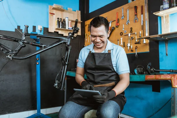 Un mecánico de bicicleta se sienta usando una tableta digital para navegar —  Fotos de Stock