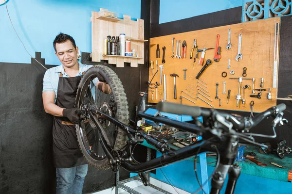 A bicycle mechanic in apron installs wheels when assembling a bicycle frame — Stock fotografie