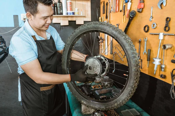 Un mecánico de bicicleta en delantal sostiene el volante libre mientras lo instala en la rueda de la bicicleta —  Fotos de Stock