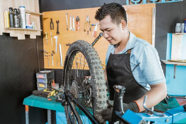 Mecánico de bicicleta masculina en delantal aprieta la rueda mientras soluciona el problema —  Fotos de Stock