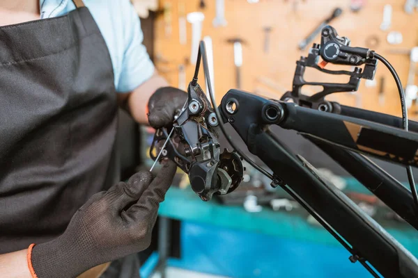 A mechanics hand in gloves pulls a cable while adjusting the rear derailleur — Stock Fotó