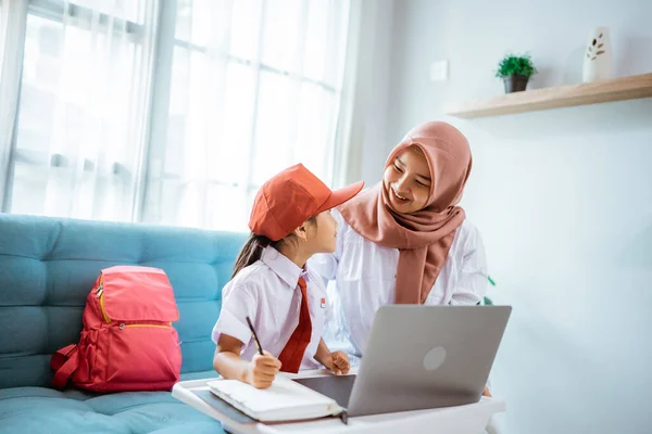 Asian muslim primary student with mother sitting together doing homework at home — Stockfoto