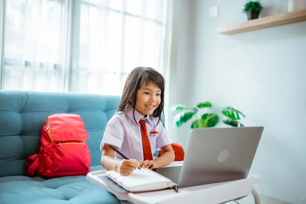 Eerste klas scholier met uniform tijdens online klas studie met leraar thuis — Stockfoto