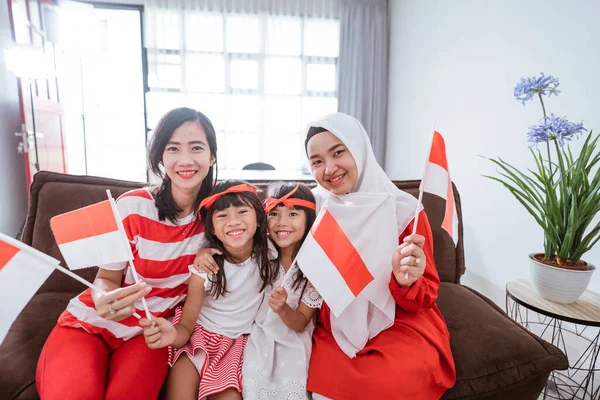 Ibu dan anak merayakan kemerdekaan indonesia hari di rumah mengenakan merah dan putih dengan bendera indonesia — Stok Foto