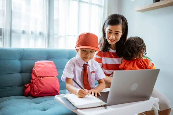 アジア系の母親は娘が自宅でオンライン授業で勉強するのを手伝い — ストック写真
