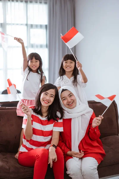 Ibu dan anak merayakan kemerdekaan indonesia hari di rumah mengenakan merah dan putih dengan bendera indonesia — Stok Foto
