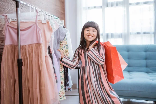 Smiling asian toddler holding a paper bag in front of dress in small boutique shop — Photo