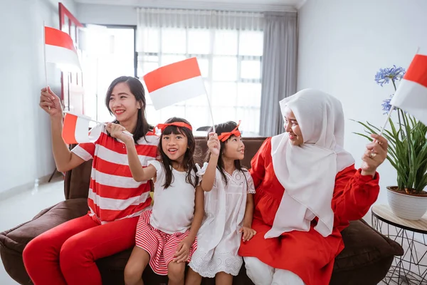 Ibu dan anak merayakan kemerdekaan indonesia hari di rumah mengenakan merah dan putih dengan bendera indonesia — Stok Foto