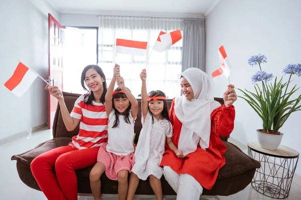 Mãe e filha celebrando o dia da independência indonésia em casa vestindo vermelho e branco com bandeira indonésia — Fotografia de Stock