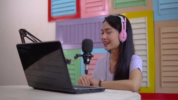 Mujer asiática usando auriculares hablando delante de micrófono con gesto de mano — Vídeo de stock