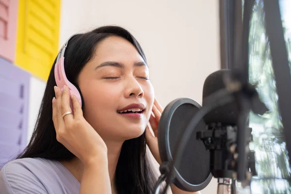 An asian female singer wearing and holding headphones while singing — Stock fotografie