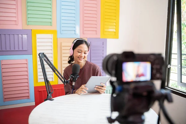 A girl wearing headphones in front of a microphone reading on a tablet while a podcast — Stockfoto