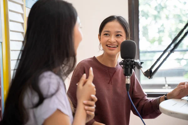 Side view of two girls laughing while having a dialogue on a podcast show using a microphone — Stockfoto