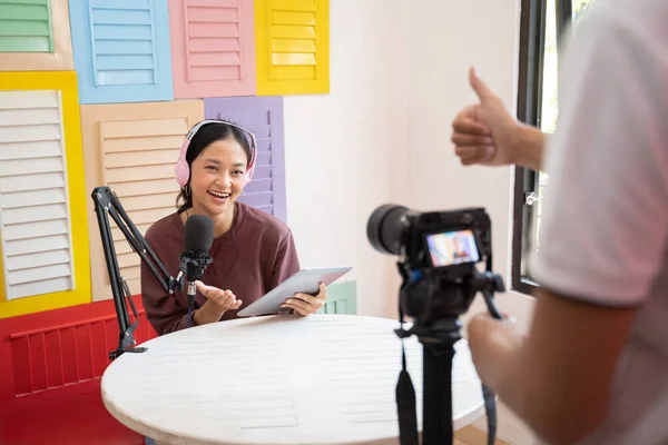 Una chica con auriculares delante de un micrófono como el camarógrafo en movimiento listo para empezar a grabar un podcast —  Fotos de Stock