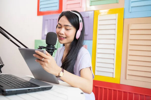 A woman reading using a pad and wearing headphones talking in front of a microphone — Φωτογραφία Αρχείου