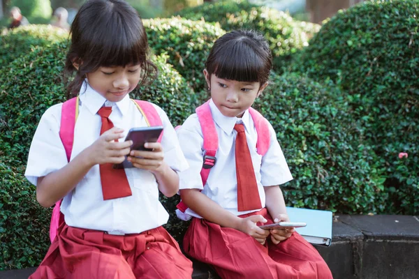 Asian primary student using mobile phone in school park — Stock Photo, Image