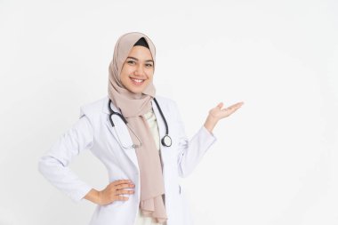 Başörtüsü takmış gülümseyen kadın doktor kameraya boş bir şekilde bakıyor.