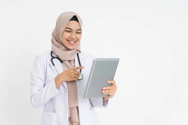 Завуальована жінка-лікар в білій формі костюма посміхається з вказівкою пальця при погляді на екран майданчика з простором — стокове фото