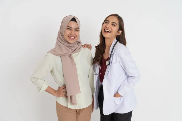 Uśmiechnięta kobieta w chustce i piękna lekarka szczęśliwie patrząca w kamerę stojąc obok siebie — Zdjęcie stockowe