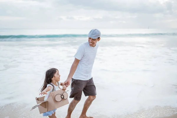 Pai e criança correndo com brinquedo avião de papelão na praia — Fotografia de Stock