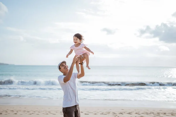 Apa ringatja a kislányát a levegőbe a parton, jól érzik magukat együtt. — Stock Fotó