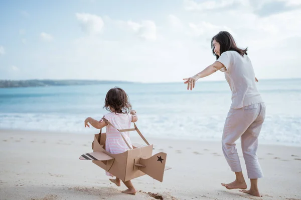 Garoto correndo na praia brincar com avião de brinquedo de papelão com a mãe — Fotografia de Stock