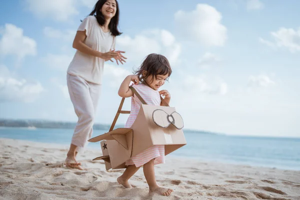 Garoto correndo na praia brincar com avião de brinquedo de papelão com a mãe — Fotografia de Stock