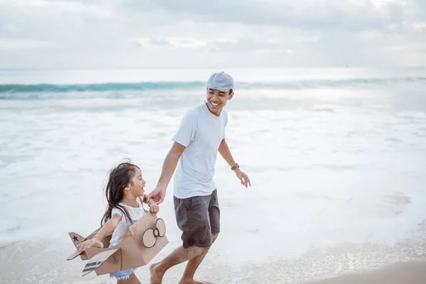 Pai e criança correndo com brinquedo avião de papelão na praia — Fotografia de Stock