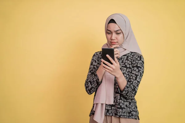Verschleierte Frau blickt mit besorgtem Gesichtsausdruck auf Bildschirm, während sie ein Smartphone benutzt — Stockfoto