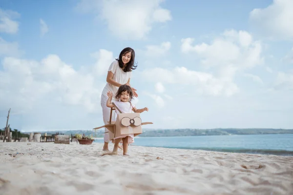 Garoto correndo na praia brincar com avião de brinquedo de papelão com a mãe — Fotografia de Stock