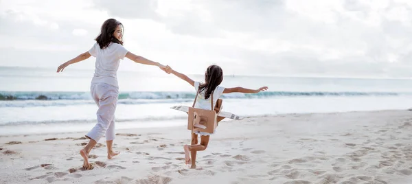 Mãe e filha brincando com avião de papelão na praia juntos — Fotografia de Stock