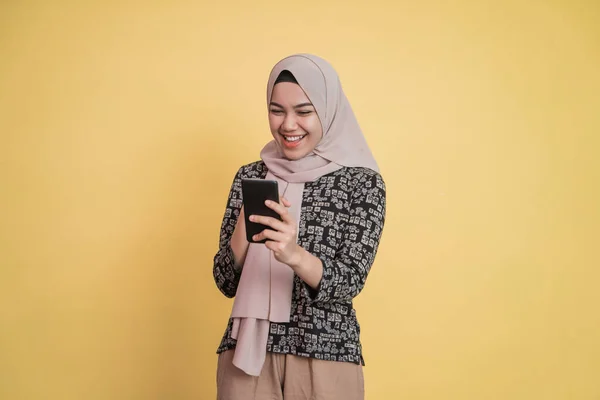 Ασιατική καλυμμένη γυναίκα κοιτάζοντας την οθόνη, ενώ χρησιμοποιώντας ένα smartphone με χαρούμενη έκφραση — Φωτογραφία Αρχείου