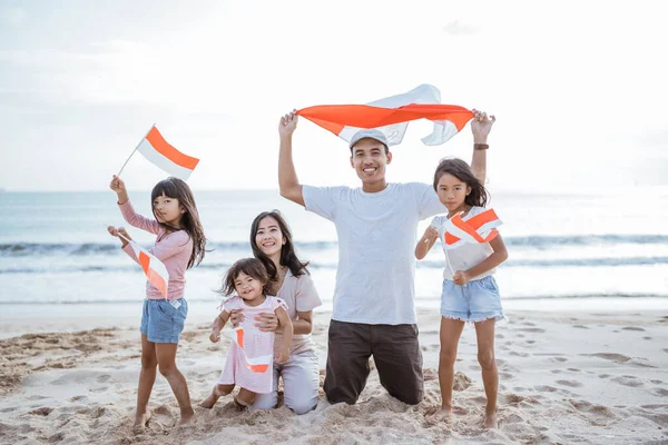 Vzrušený indonéský rodinný příznivec s indonéskou vlajkou na pláži společně — Stock fotografie