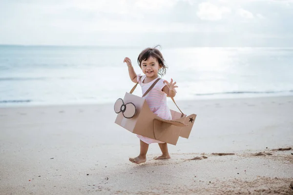 Bambino che corre in spiaggia gioca con un aeroplano giocattolo di cartone — Foto Stock