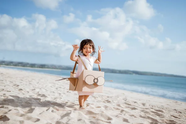 Bambino che corre in spiaggia gioca con un aeroplano giocattolo di cartone — Foto Stock