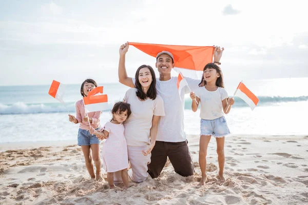 Entusiasta sostenitore della famiglia indonesiana con bandiera indonesiana in spiaggia insieme — Foto Stock