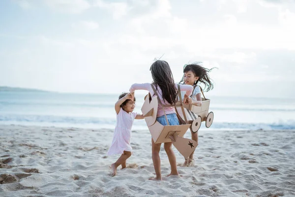 Broer en zus en meisje vriend spelen met karton vliegtuig en auto op het strand — Stockfoto