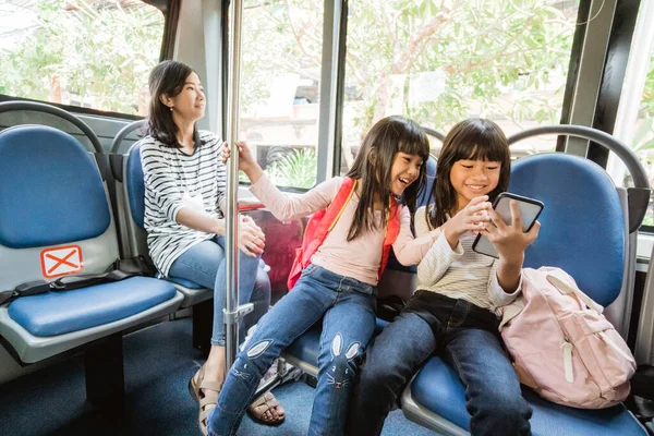 Asian student girl using smartphone while riding public bus together on their way to the school — Stock Photo, Image