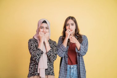 İki Asyalı kız korkmuş ifadeye bakıyor ve kamerayı işaret ediyor.