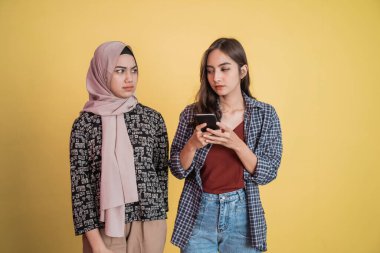 Kendine güvenen güzel bir kadın cep telefonu kullanıyor ve peçeli bir kadın şüpheli bir şekilde ona bakıyor.