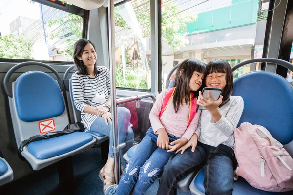 Азіатська студентка використовує смартфон під час їзди на громадському автобусі разом на шляху до школи — стокове фото