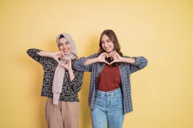 İki kadın el hareketleriyle kameraya gülümsüyor. Kopyalama alanı ile aşk işareti oluşturuyorlar.