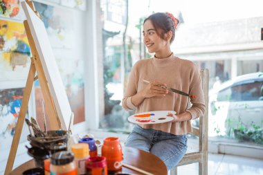 Asyalı kadın ressam atölyesinde tuvale resim yapıyor.