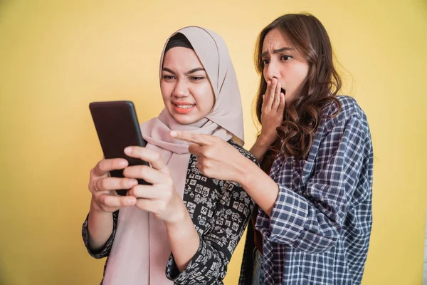 Nahaufnahme einer Frau mit Kopftuch und einer Frau mit langen Haaren benutzen ein Handy und sind überrascht, als sie den Telefonbildschirm sehen — Stockfoto