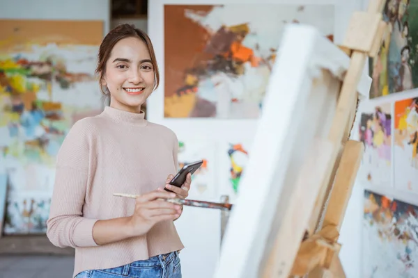 Kvinnlig konstnär målning hålla telefonen medan du arbetar — Stockfoto