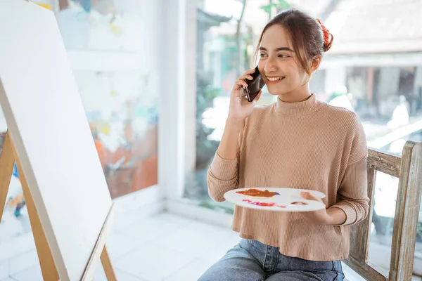 Vrouw kunstenaar schilderij op doek tijdens het praten op haar telefoon — Stockfoto